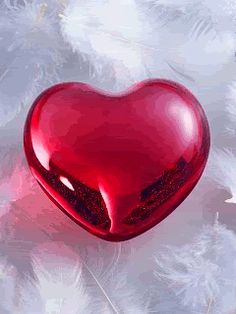 a red glass heart sitting on top of feathers