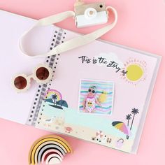 a camera, sunglasses, and photo album on a pink surface