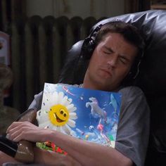 a man sleeping on a chair holding a book with a smiley face drawn on it