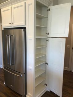 a refrigerator and pantry in a kitchen with hardwood floors, white cabinets and stainless steel appliances