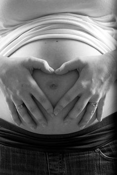 a pregnant woman's stomach with her hands in the shape of a heart