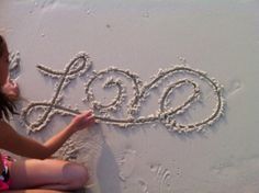 a girl is writing the word love in sand