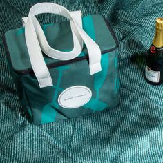 a bottle of wine sitting next to a bag on top of a bed with blue sheets