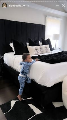 a toddler standing on the edge of a black and white bed in a bedroom