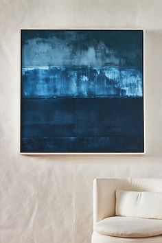 an abstract painting hangs on the wall above a white chair