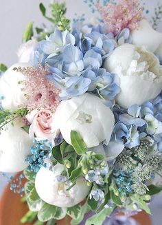 a bouquet of white and blue flowers on an orange vase with greenery around it