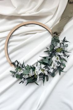 a wreath with flowers and greenery is laying on a white sheeted bed spread