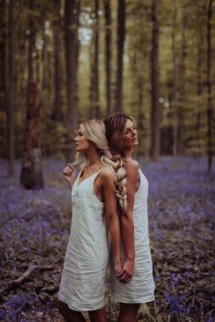 two women standing next to each other in the woods with their arms around each other