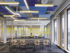 an empty conference room with yellow and blue lighting on the ceiling, along with chairs and tables