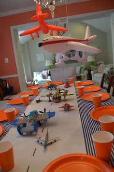 an airplane is flying over the table with orange cups and plates on it, as well as toy airplanes