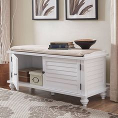 a white bench with books on top of it in front of two framed pictures and a rug