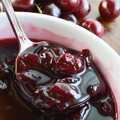 a spoon full of cherries sitting on top of a white bowl filled with liquid