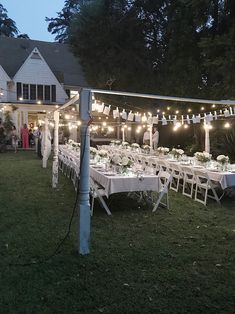 an outdoor wedding reception with string lights and white tablecloths on the tables, in front of a large house