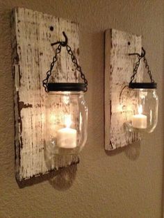 two mason jars are hanging on the wall with candles in them and one is holding a lit candle