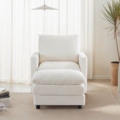 a white chair sitting in front of a window next to a tall potted plant