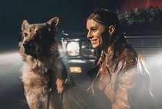 a woman sitting next to a dog in front of a car on the street at night