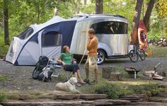 two people and a dog in front of a camper with an rv parked next to it