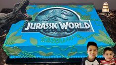 two young boys standing in front of a cake with the words jurassic world on it