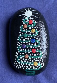 a painted rock with a christmas tree on it's side and dots all over the surface