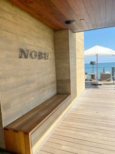 a wooden bench sitting on the side of a building next to an umbrella covered beach