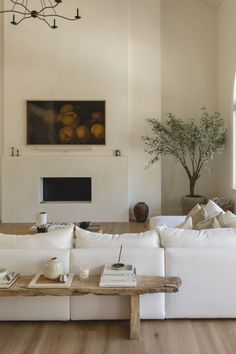 a living room filled with white couches and a wooden table in front of a fire place