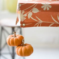 two small pumpkins hanging from the side of a table with an orange flowered cloth