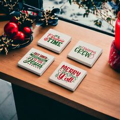 four coasters sitting on top of a wooden table next to a vase and christmas tree