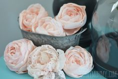 some pink flowers are sitting on a blue table and one is in a metal bowl