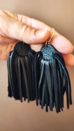 a pair of black tasselled earrings with gold accents on each earring is held in someone's hand