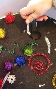 a child's hand holding a pair of scissors over a black surface covered in colorful beads