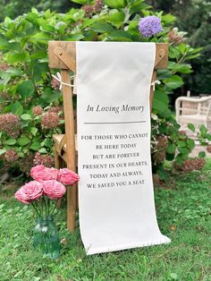 a memorial sign sitting on top of a grass covered field next to flowers and a wooden bench