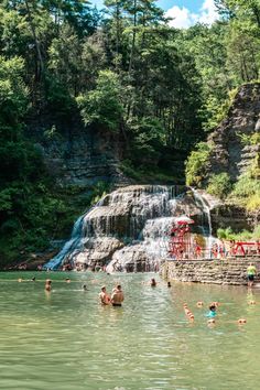 people are swimming in the water near a waterfall