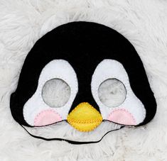 a black and white penguin mask sitting on top of a fluffy white surface with two holes in the middle