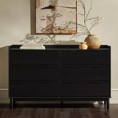 a black dresser with two vases and a painting on the wall in the background