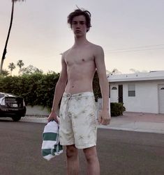 a shirtless man is standing in the middle of the street holding a towel and a bag