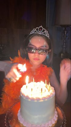 a woman wearing glasses and a tiara is blowing out candles on her birthday cake