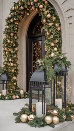 two black lanterns with christmas decorations and candles on the side of a building in front of a doorway