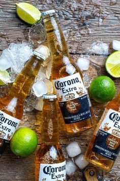 four bottles of corona extra are surrounded by ice and limes