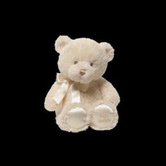 a white teddy bear with a bow on it's neck sitting in front of a black background