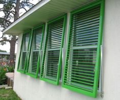 green shutters on the side of a white building with trees in the background,