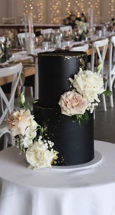 two tiered black wedding cake with white and pink flowers on the top, sitting on a round table