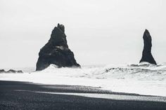 black sand beach with two large rock formations in the distance and waves crashing on it