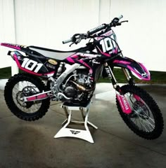 a pink and black dirt bike parked in front of a white garage door with the number ten on it