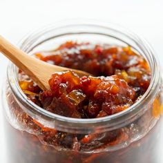 a person holding a wooden spoon in a jar filled with jam