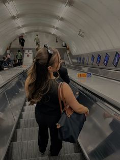 two women are riding an escalator with their backs to each other and one is carrying a purse