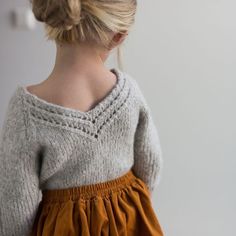 a woman with blonde hair wearing a sweater and orange skirt standing in front of a white wall