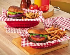 two baskets filled with hamburgers and fries sitting on top of a wooden cutting board