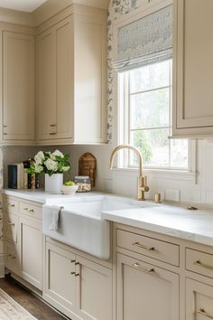 a clean kitchen with white cabinets and gold faucets on the windowsills