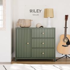 a green cabinet with a guitar on top and a lamp in the corner next to it