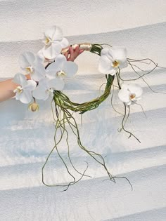 a wreath with white orchids is held by someone's hand in the sand